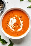 a bowl of homemade tomato Soup topped with a swirl of cream made with carrots, onion, tomatoes, basil and cream