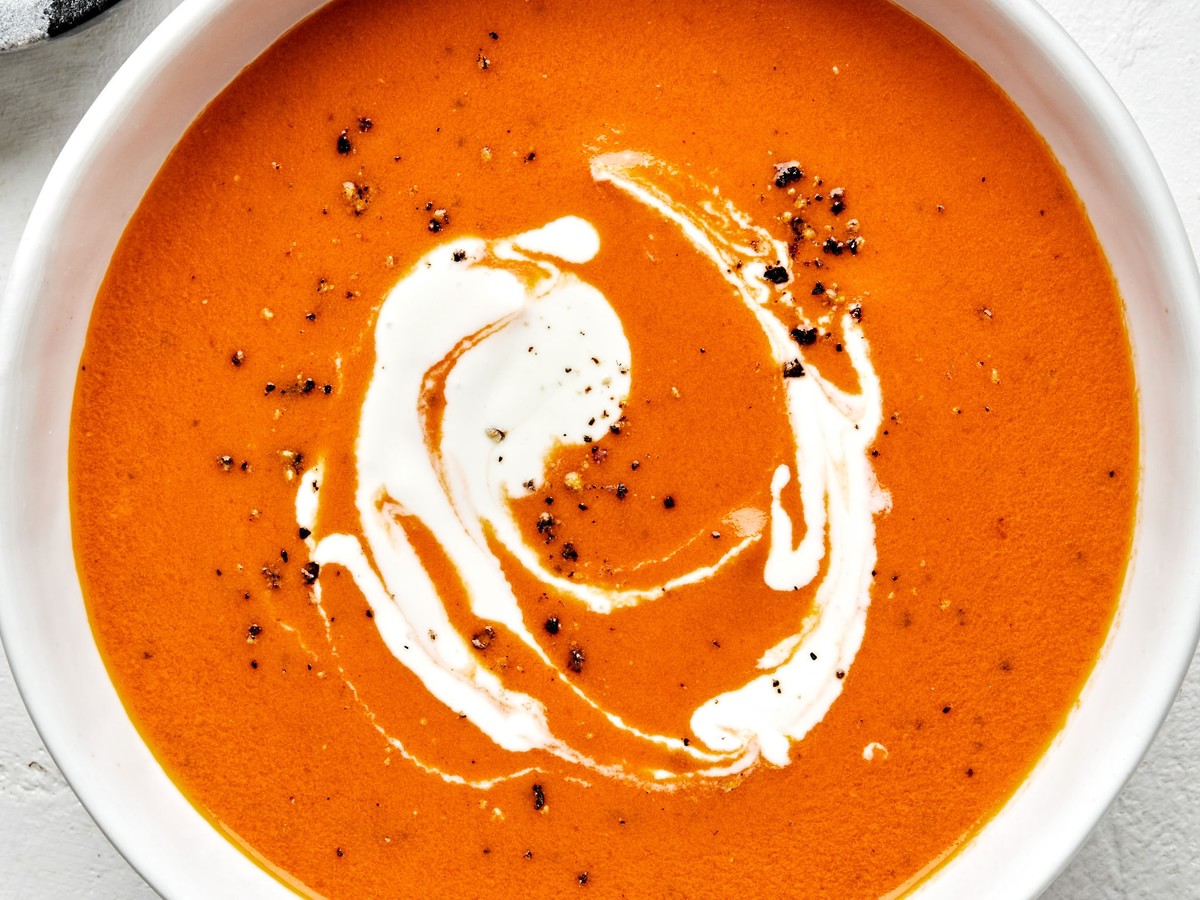 a bowl of homemade tomato bisque topped with a swirl of cream made with carrots, onion, tomatoes, basil and cream