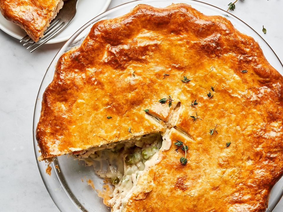 a homemade turkey pot pie filled with turkey, celery, carrot, onion & peas with a slice cut out sitting on plate next to it