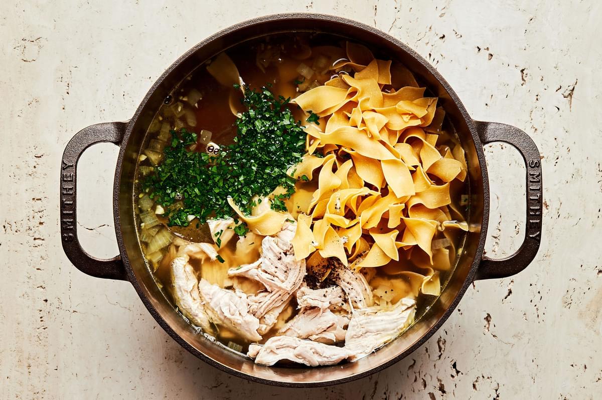 vegetables, turkey, noodles, stock and parsley in a soup pot for turkey soup