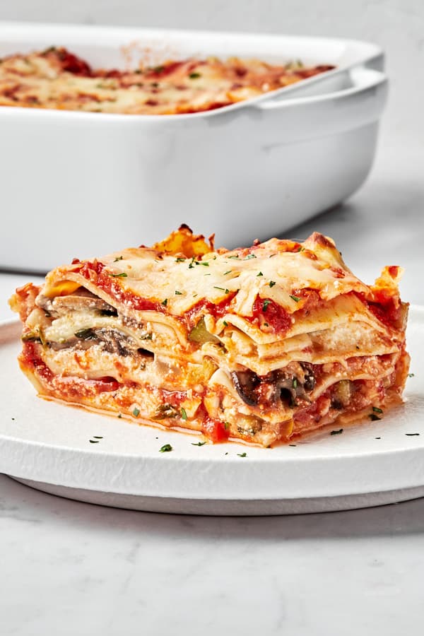 a slice of homemade vegetable lasagna on a plate next to a casserole dish of vegetable lasagna