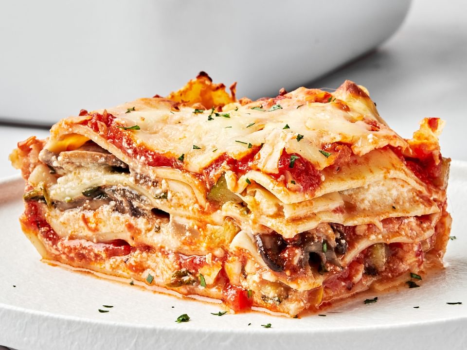 a slice of homemade vegetable lasagna on a plate next to a casserole dish of vegetable lasagna