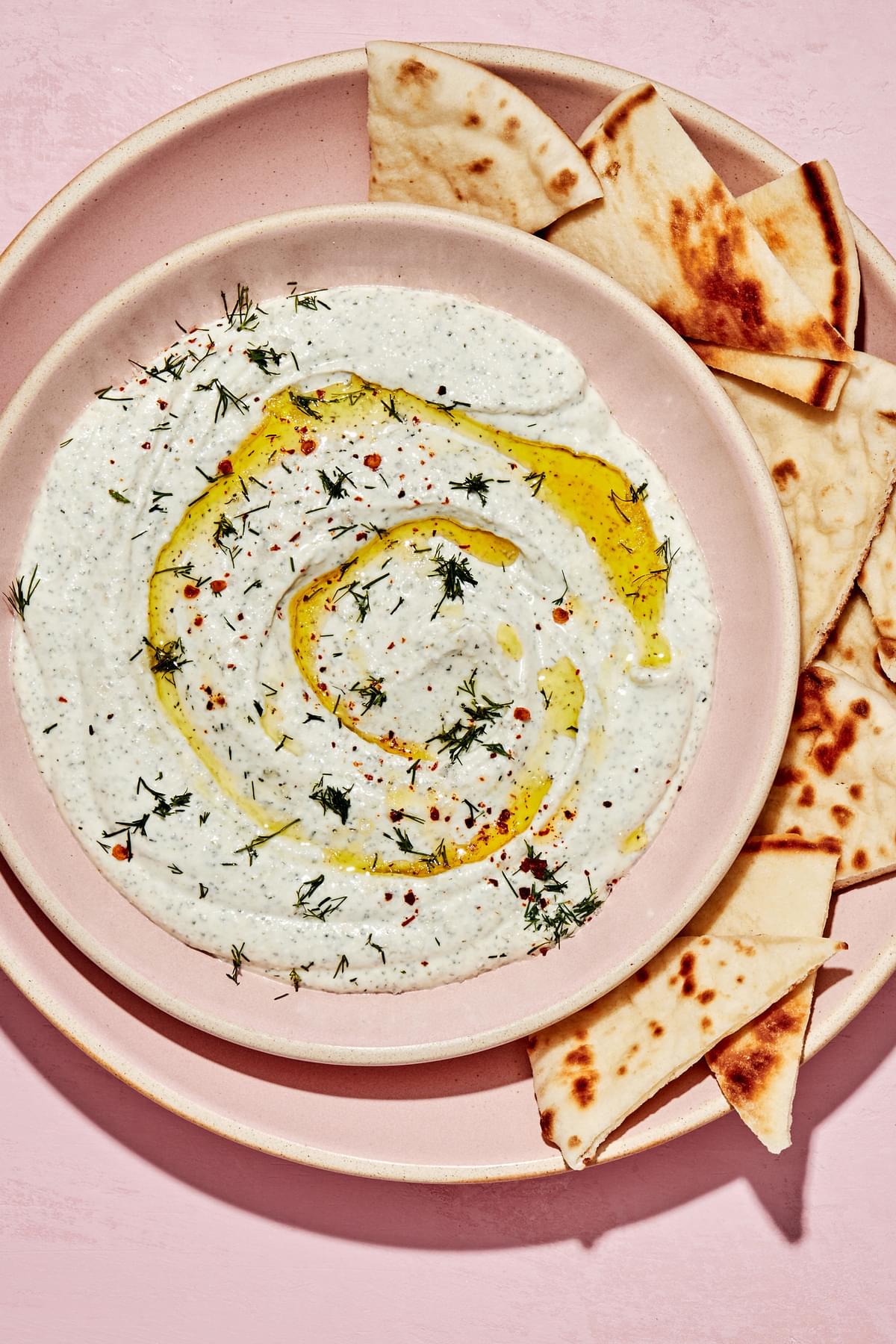 whipped feta dip made with feta, greek yogurt and spices in a serving bowl with sliced pita bread for dipping