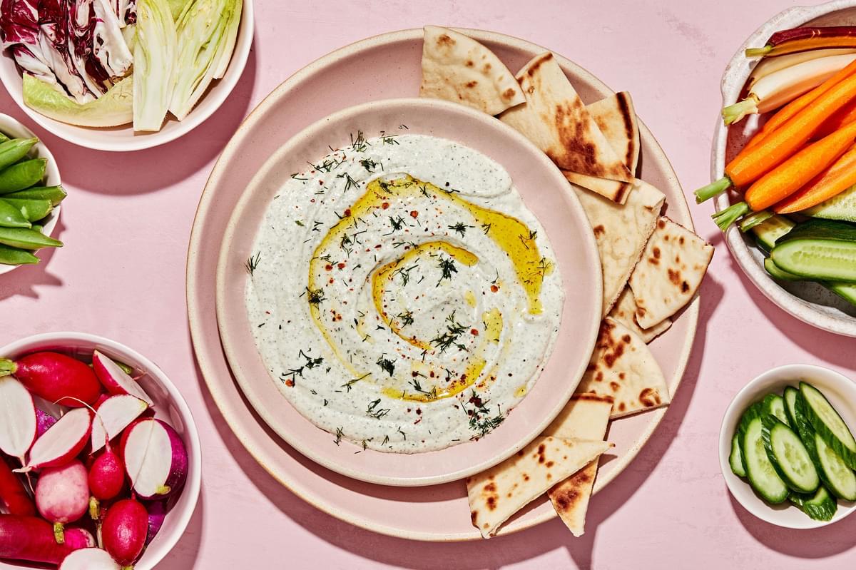whipped feta dip made with feta, greek yogurt and spices in a serving bowl surrounded by pita bread & vegetables for dipping