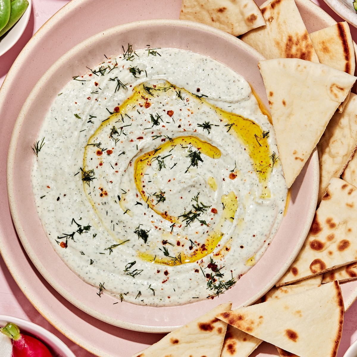 whipped feta dip in a serving bowl surrounded by sliced pita bread, and roasted and raw vegetables for dipping