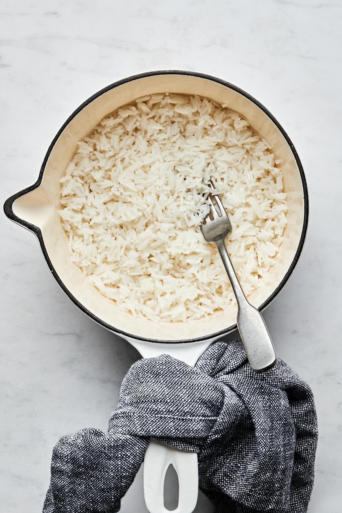 fluffy white rice in a sauce pan with a fork made with rice, water, salt and butter
