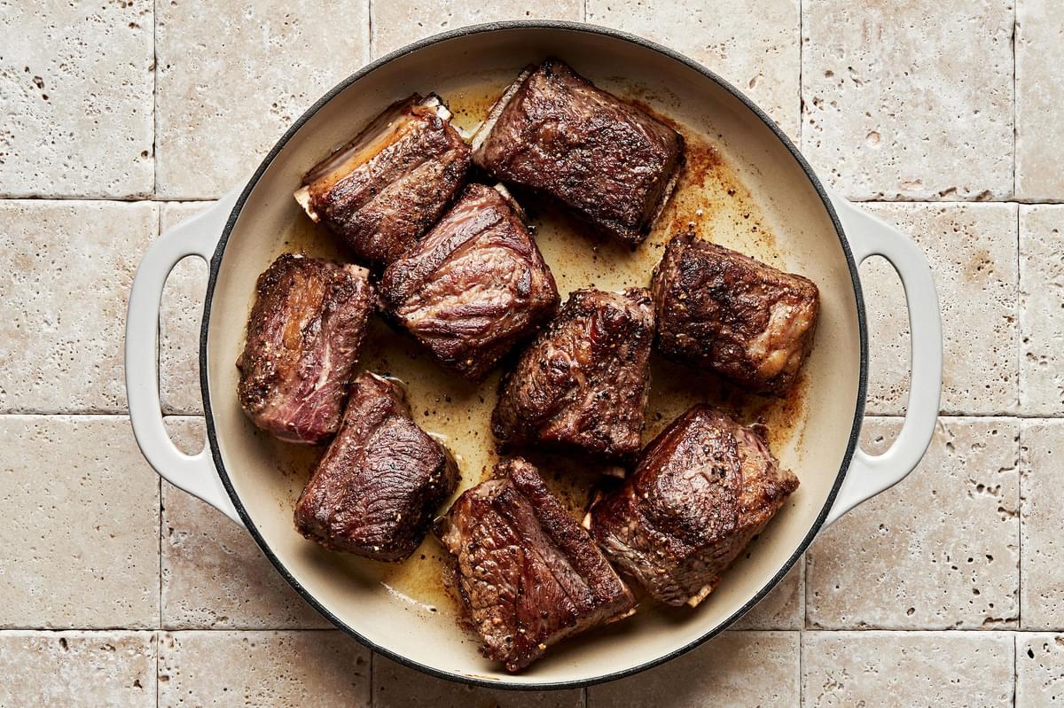short ribs seasoned with salt and pepper being browned in a dutch oven with vegetable oil