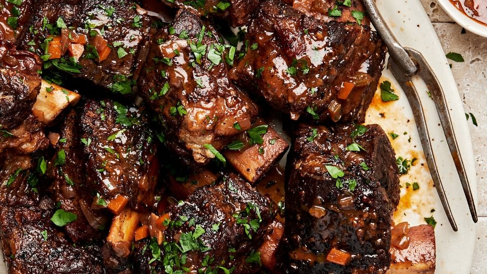 wine braised short ribs on a serving plate made with red wine, spices, celery, onion, carrots and garlic cloves