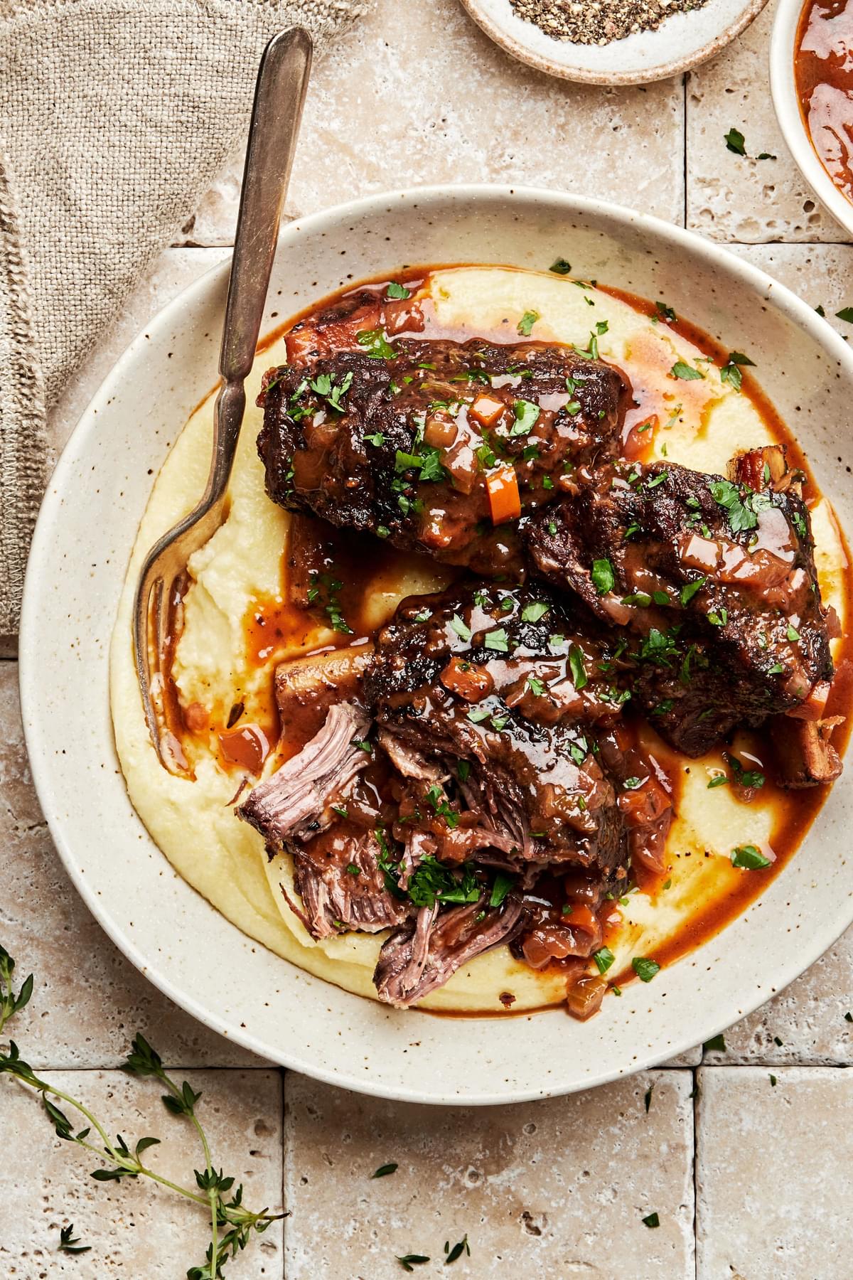 homemade wine braised short ribs in a bowl served on top of mashed potatoes and sprinkled with parsley
