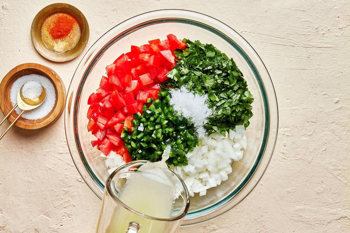 chopped tomatoes, onion, cilantro, jalapeños, salt in a mixing bowl with lime juice being poured in to make pico de Gallo