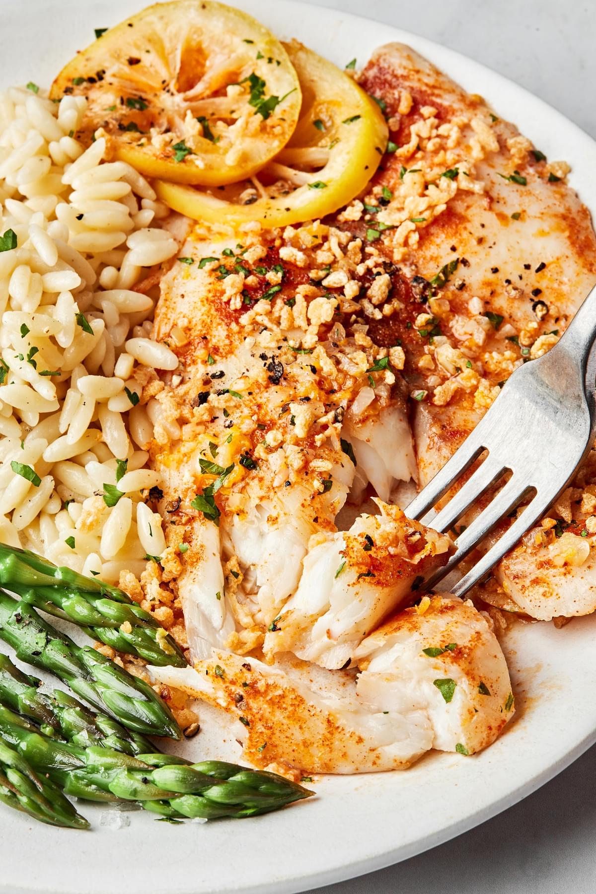 baked tilapia on a dinner plate served with brown rice and roasted asparagus