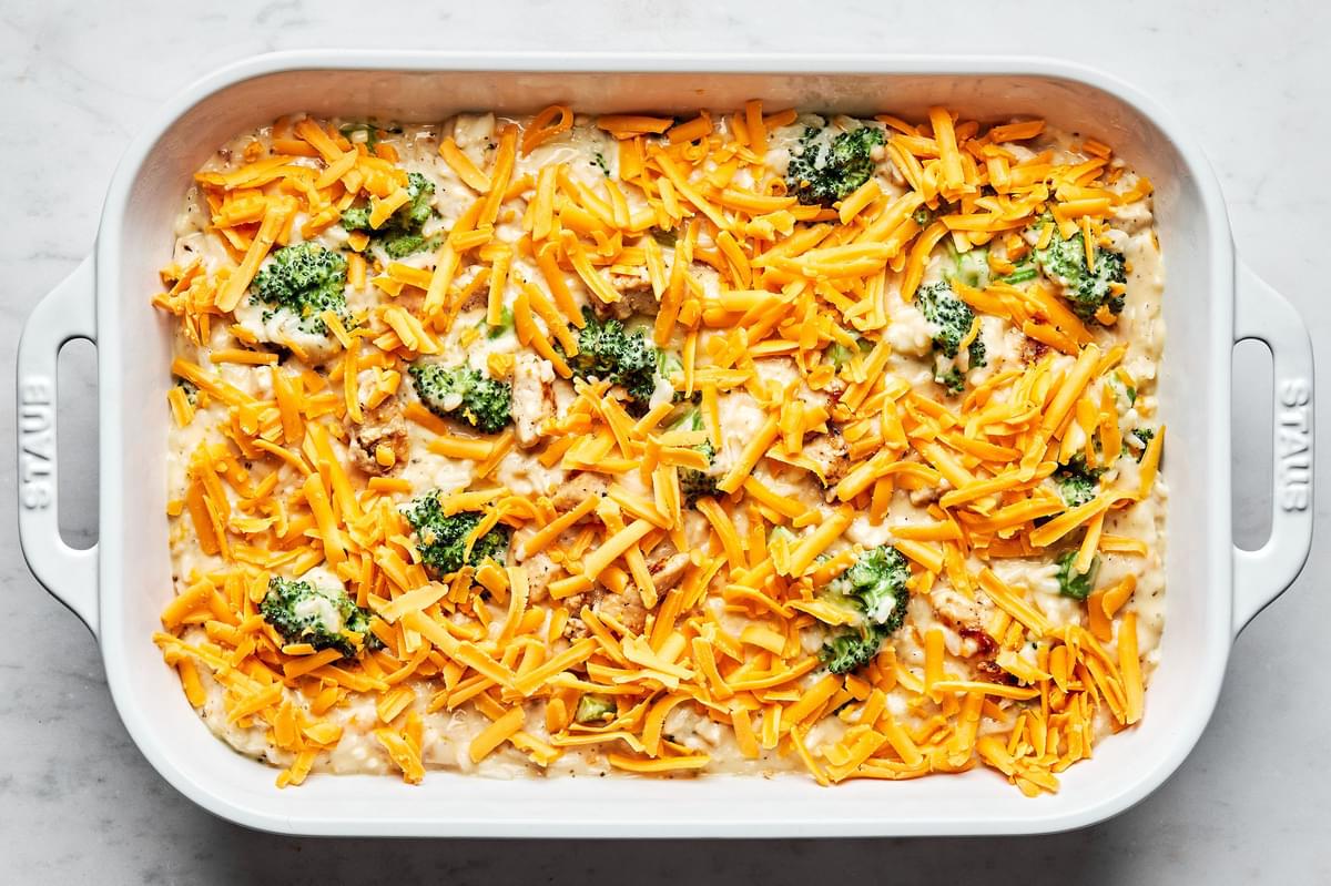 rice, chicken, broccoli and sauce mixed together in a casserole baking dish topped with cheese