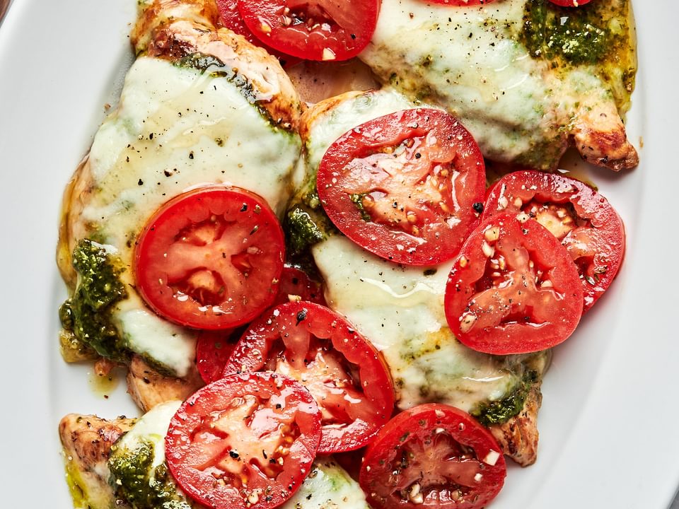 chicken caprese on a serving platter topped with pesto, melted mozzarella, roma tomatoes and drizzled with honey