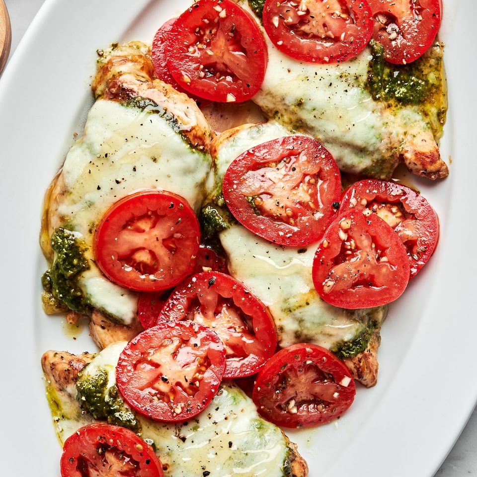 chicken caprese on a serving platter topped with pesto, melted mozzarella, roma tomatoes and drizzled with honey