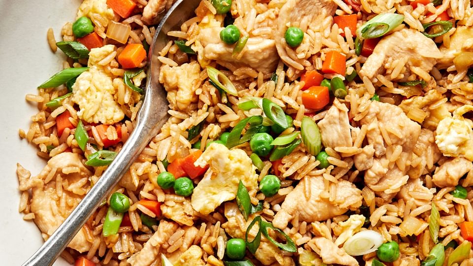 a bowl of chicken fried rice made with carrots, onions, peas, green onions, eggs, soy sauce, coconut aminos and sesame oil