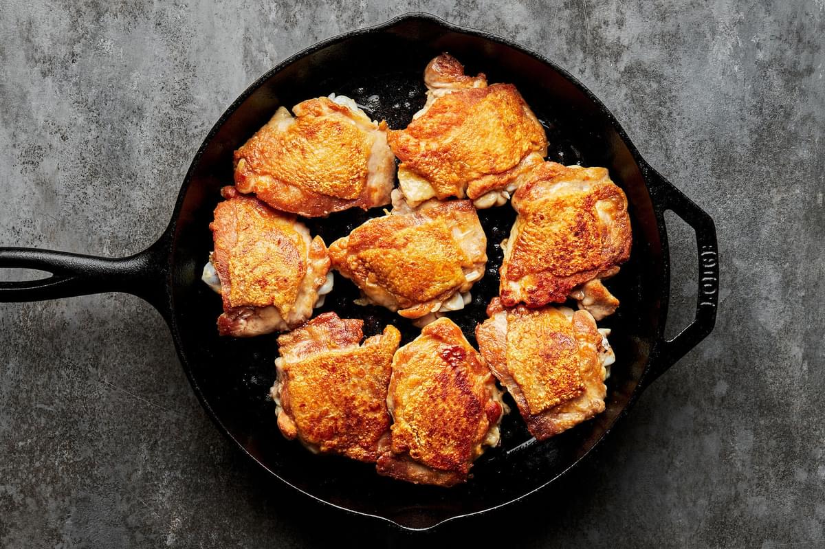 bone-in, skin-on chicken thighs seasoned with salt being cooked in olive oil in a skillet until golden brown