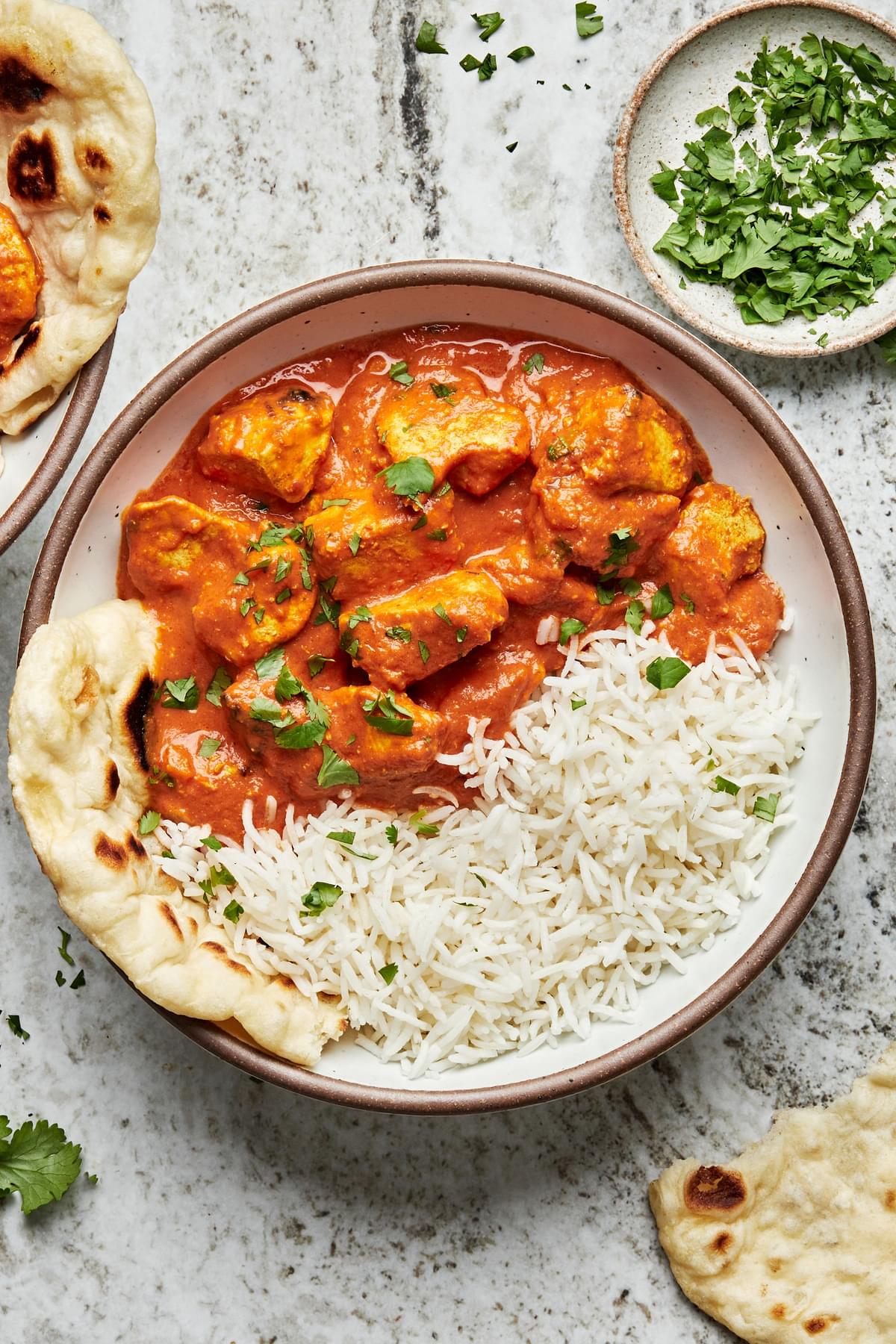 A bowl of homemade chicken tikka masala and white rice sprinkled with fresh cilantro  being served with naan