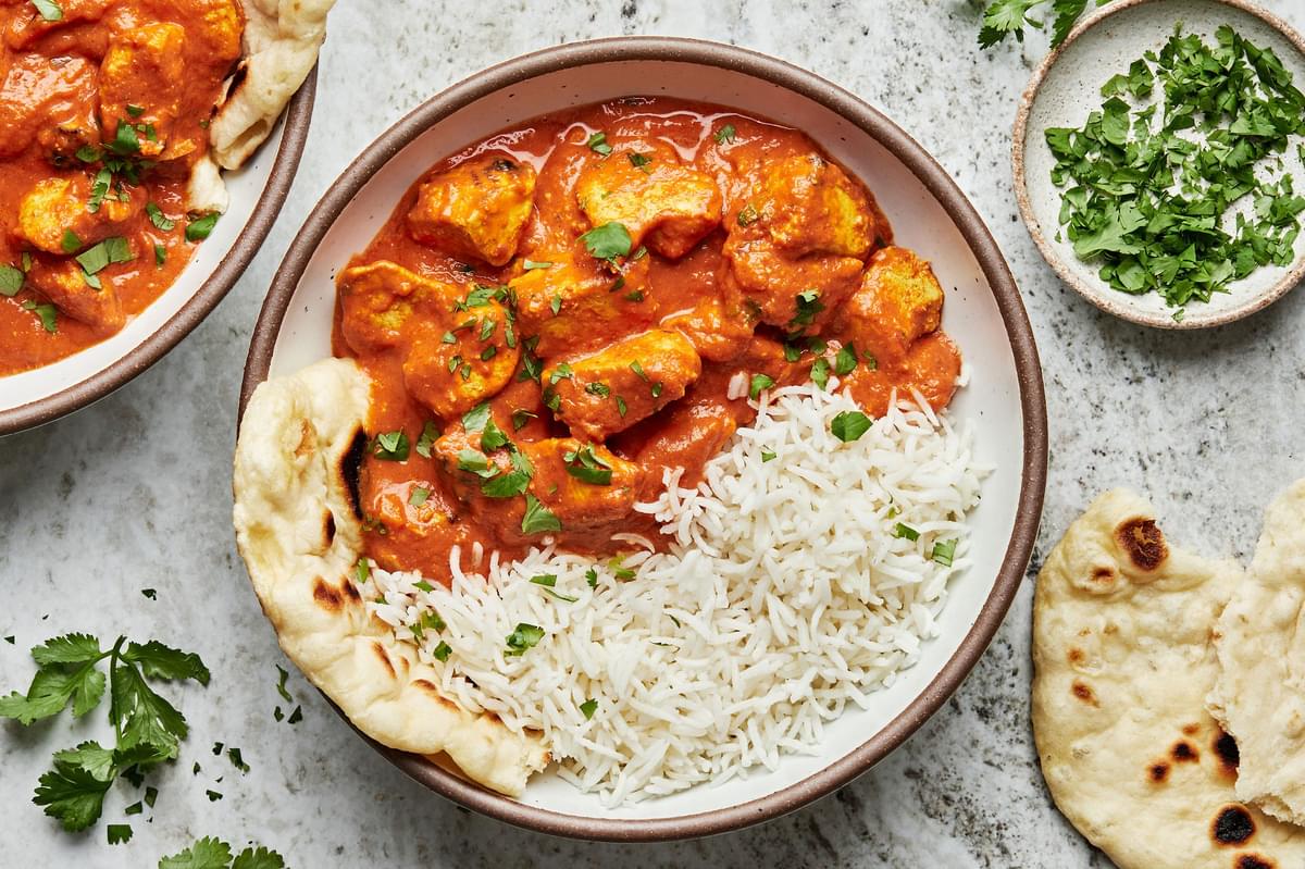 A bowl of homemade chicken tikka masala and white rice sprinkled with fresh cilantro being served with naan