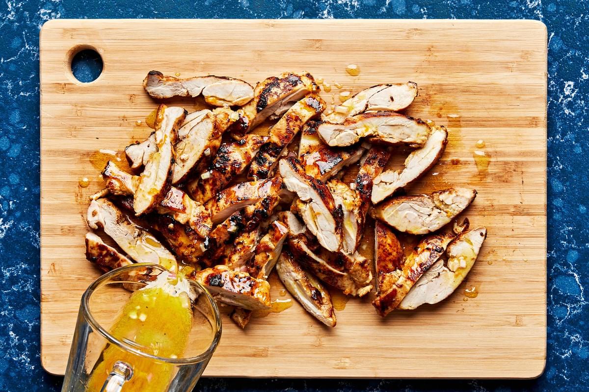 cooked citrus chicken sliced on a cutting board being drizzled with citrus sauce