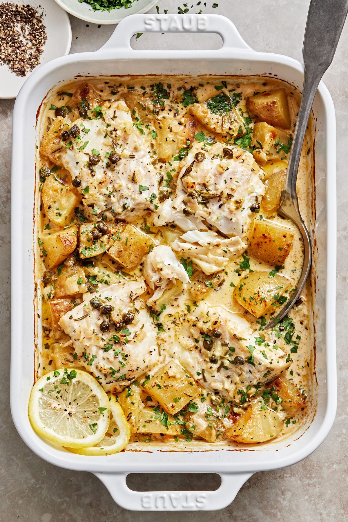 Cod and Potatoes in Rosemary Cream Sauce sprinkled with parsley in a baking dish with a serving spoon