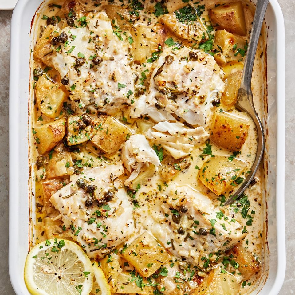 Cod and Potatoes in Rosemary Cream Sauce sprinkled with parsley in a baking dish with a serving spoon