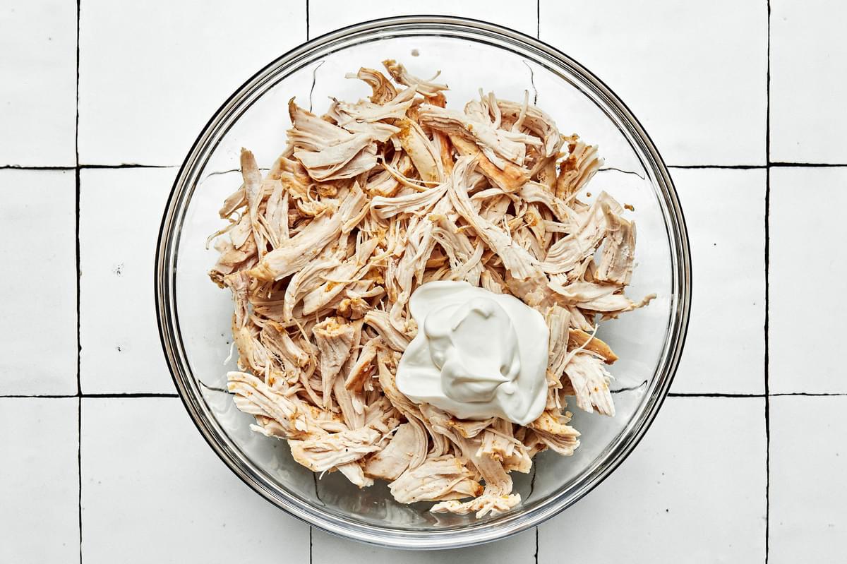 cooked shredded chicken in a large glass mixing bowl with sour cream