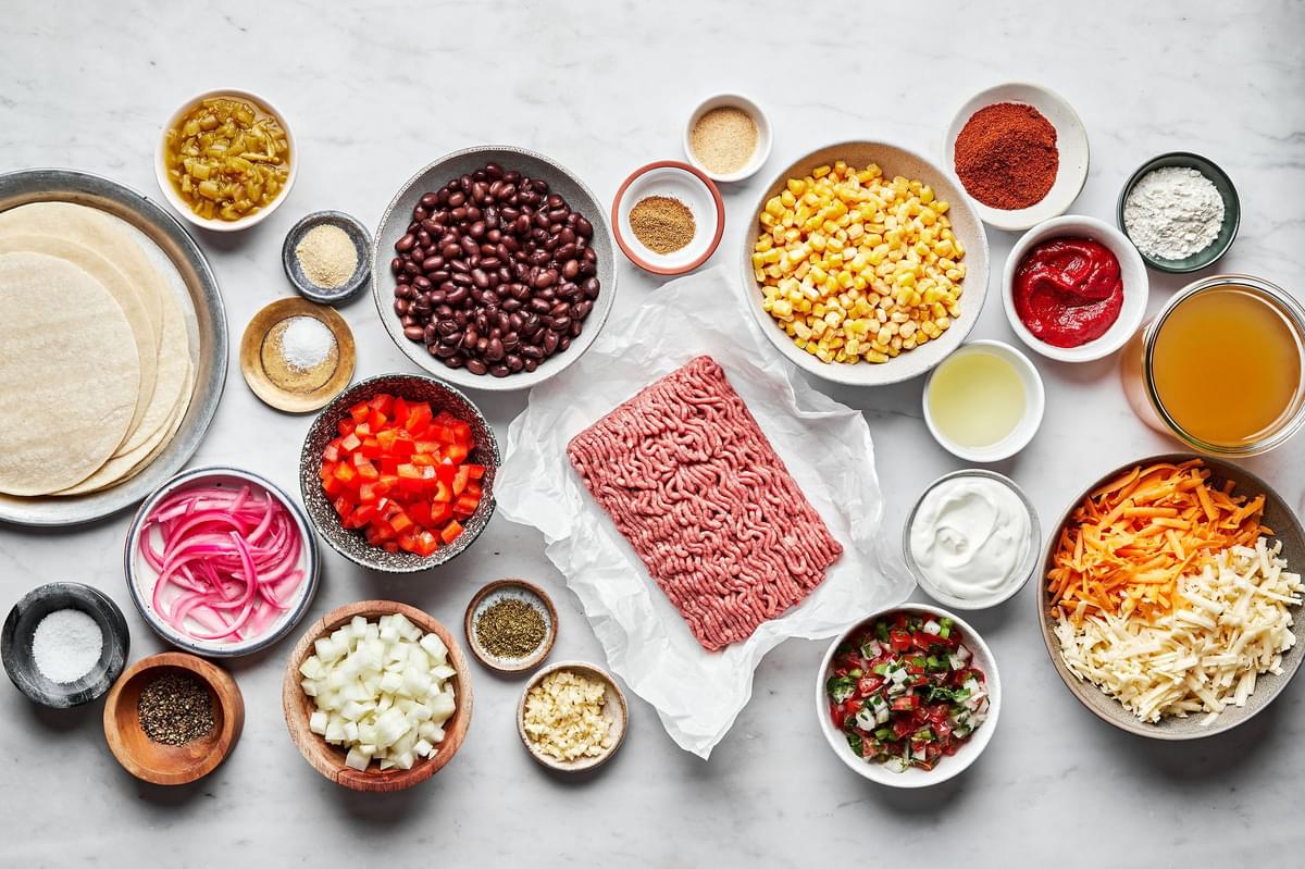 ingredients for enchilada casserole in prep bowls: ground beef, spices, onion, pepper, chiles, black beans and corn