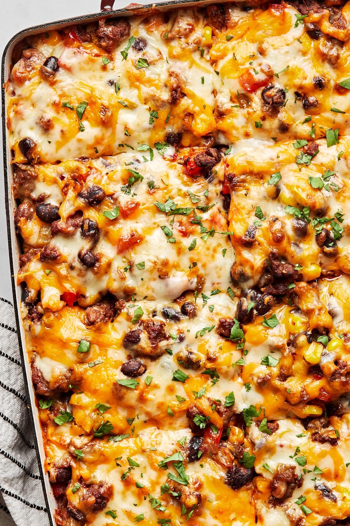 enchilada casserole in a baking dish made with ground beef, black beans, corn, peppers, onions, chiles and cheese