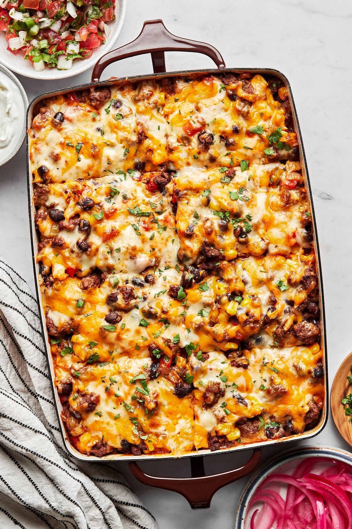 enchilada casserole in a baking dish made with ground beef, black beans, corn, peppers, onions, chiles and cheese