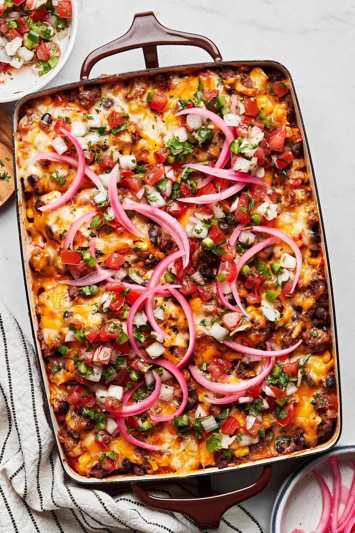 homemade enchilada casserole in a baking dish topped with pico de gallo and pickled onions