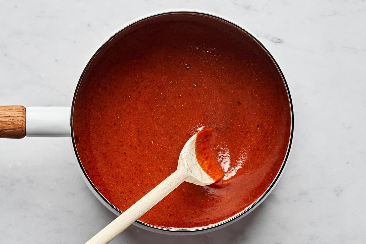 enchilada sauce in a pot spiced with chili powder, garlic powder, onion powder, cumin, oregano & tomato paste