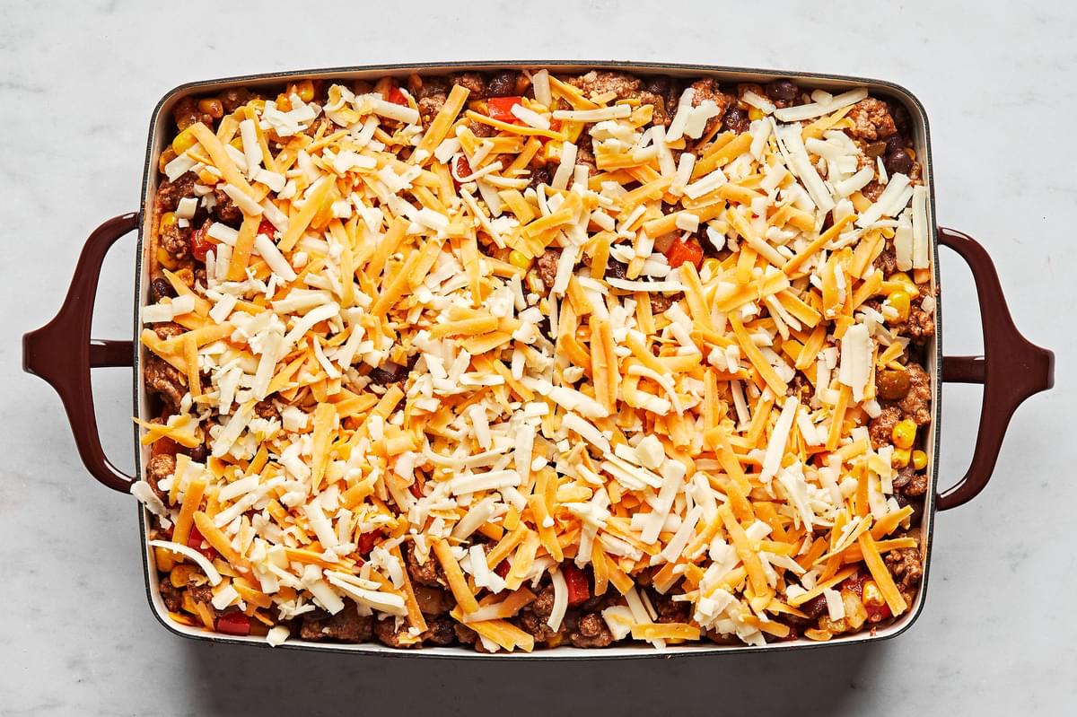 enchilada casserole topped with shredded cheese in a casserole dish read to be baked