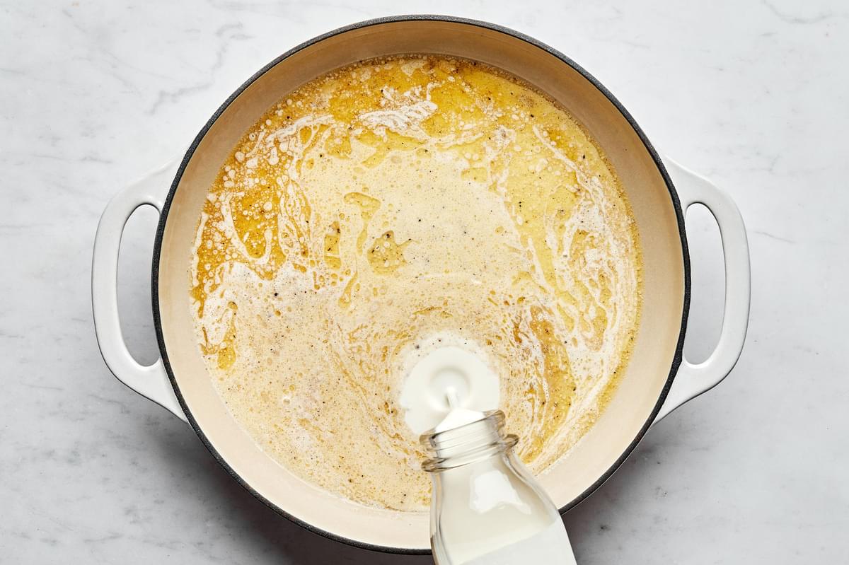 Heavy cream being poured into butter in a skillet to make Alfredo sauce.