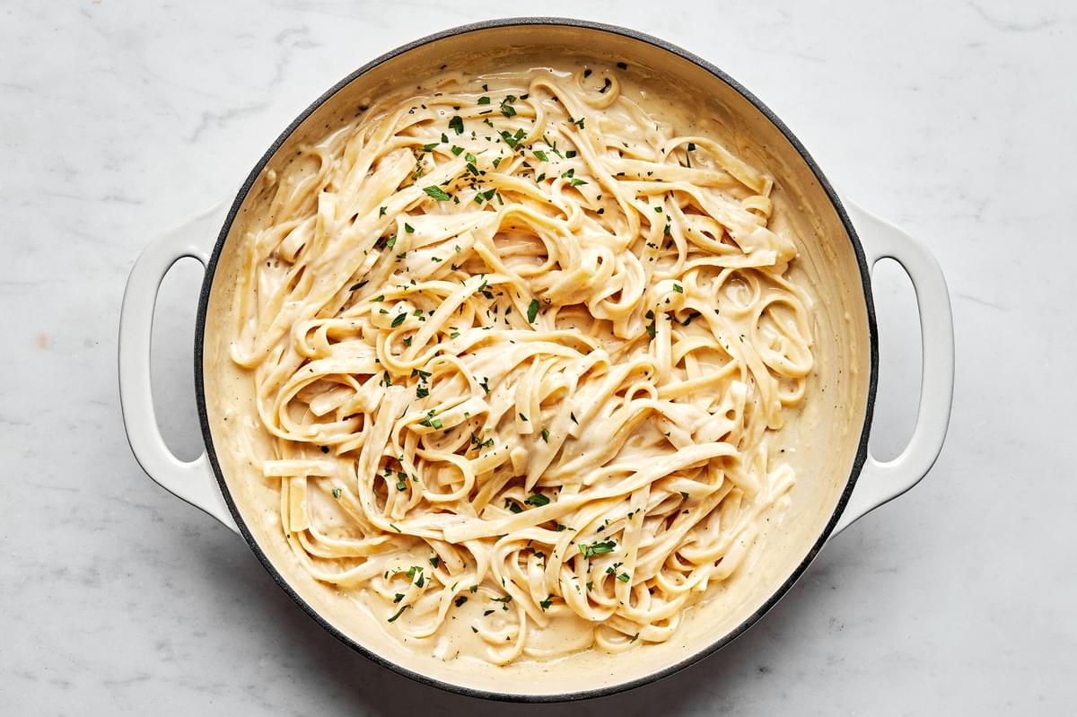 Homemade fettuccine alfredo in a skillet sprinkled with fresh parsley