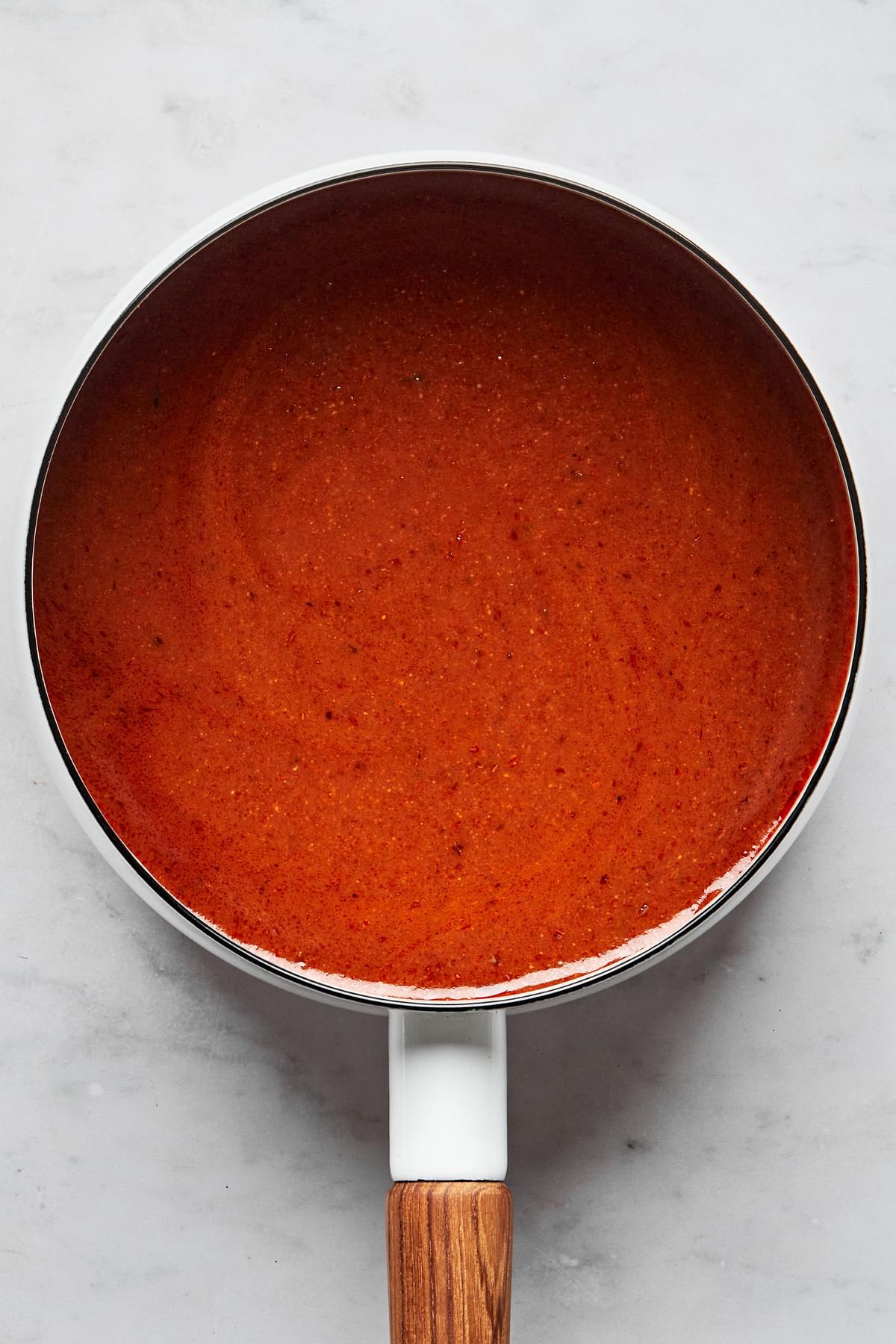 homemade enchilada sauce in a pot spiced with chili powder, garlic powder, onion powder, cumin, oregano, and tomato paste