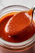 homemade enchilada sauce being spooned out of a glass jar