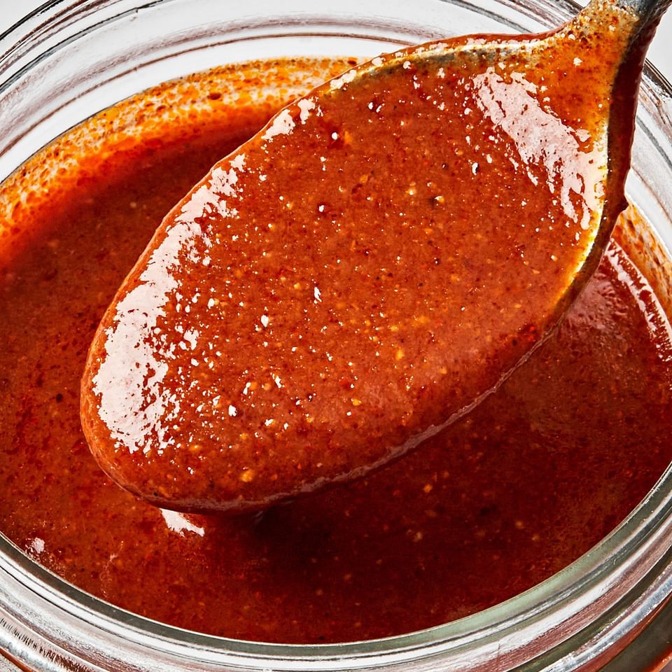 homemade enchilada sauce being spooned out of a glass jar