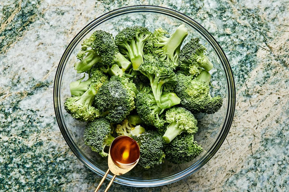 broccoli being tossed with olive oil and salt in a large glass bowl