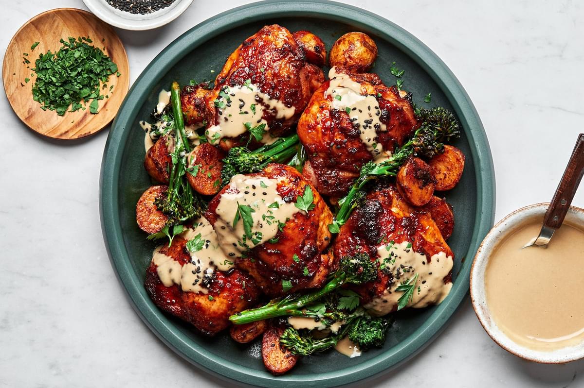 honey harissa chicken, potatoes and broccoli on a serving platter drizzled with tahini sauce