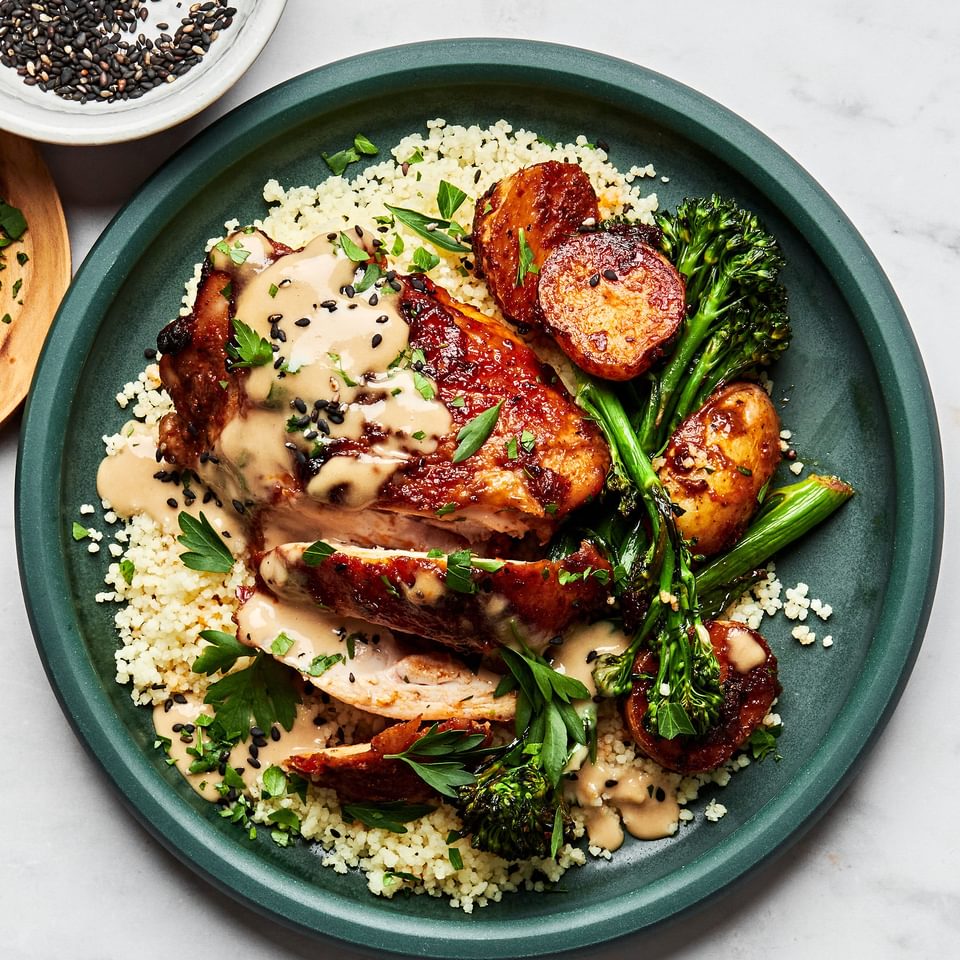 Honey harissa chicken, potatoes and broccoli served over couscous and drizzled with tahini sauce