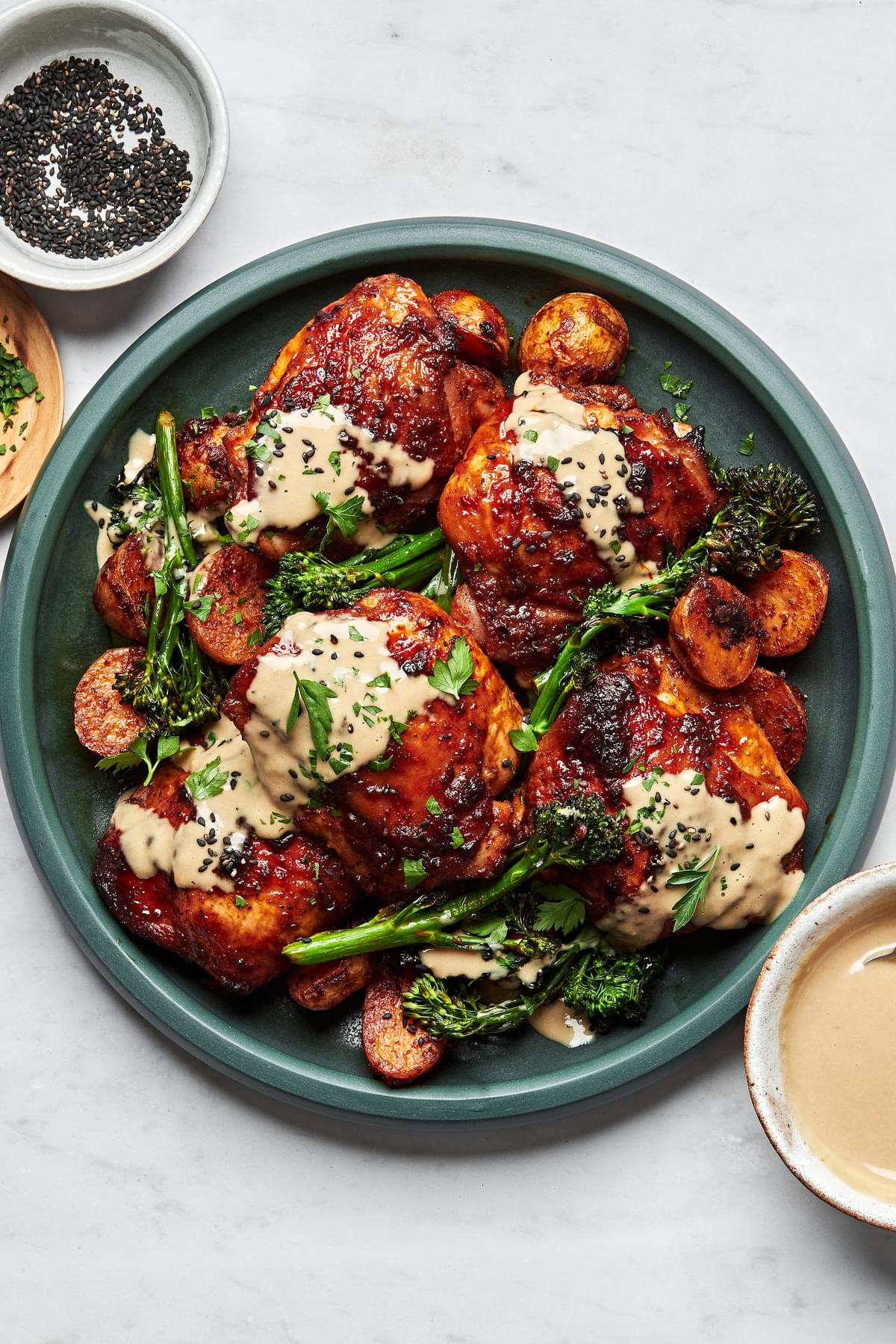 honey harissa chicken, potatoes and broccoli on a serving platter drizzled with tahini sauce