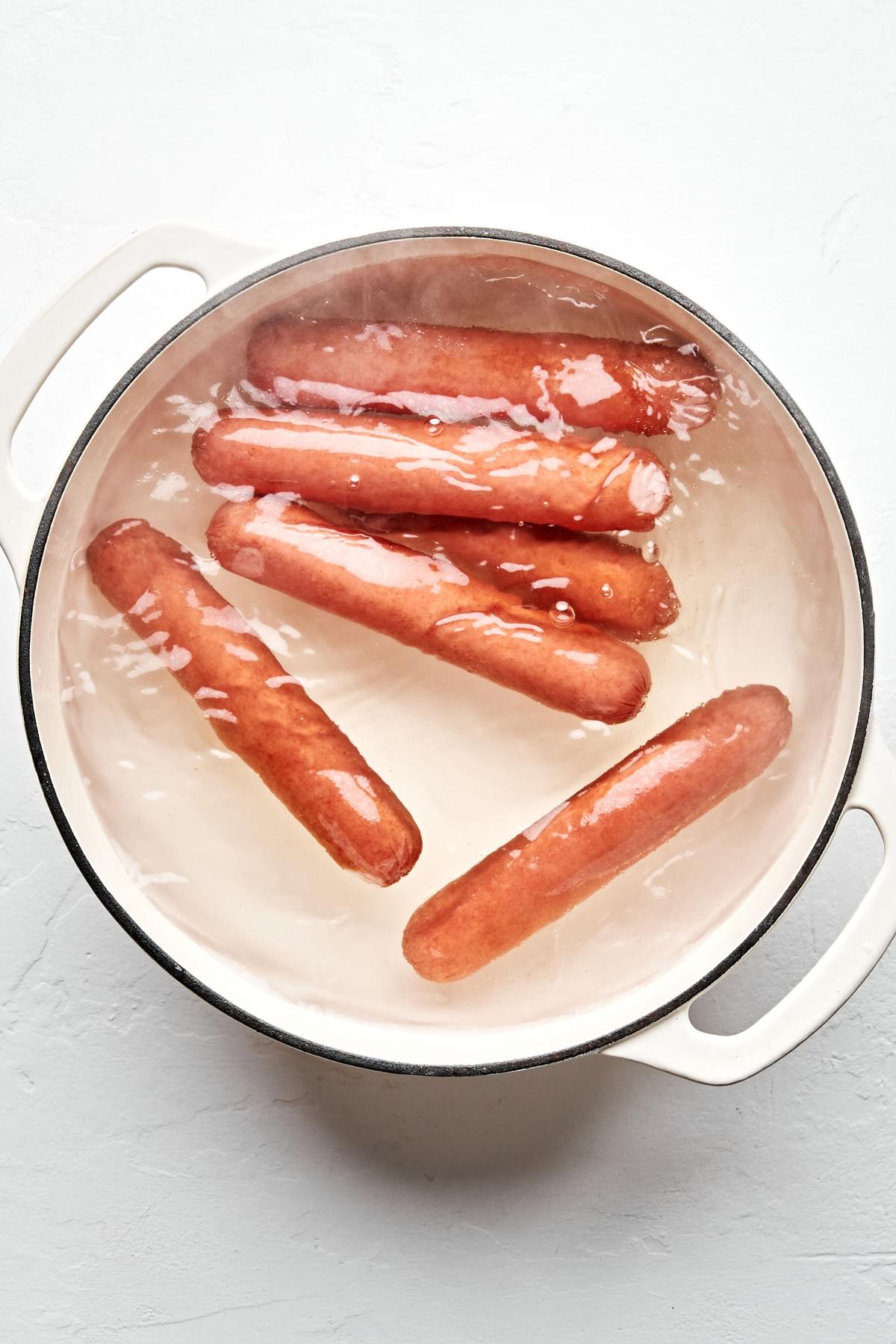 6 hot dogs being cooked in boiling water