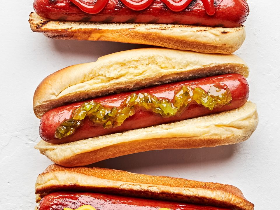 3 homemade hot dogs in buns one topped with ketchup, one with mustard and one with relish