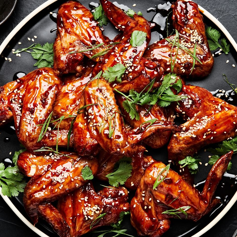 Korean Style Baked chicken wings sprinkled with cilantro, green onions and sesame seeds on a serving platter