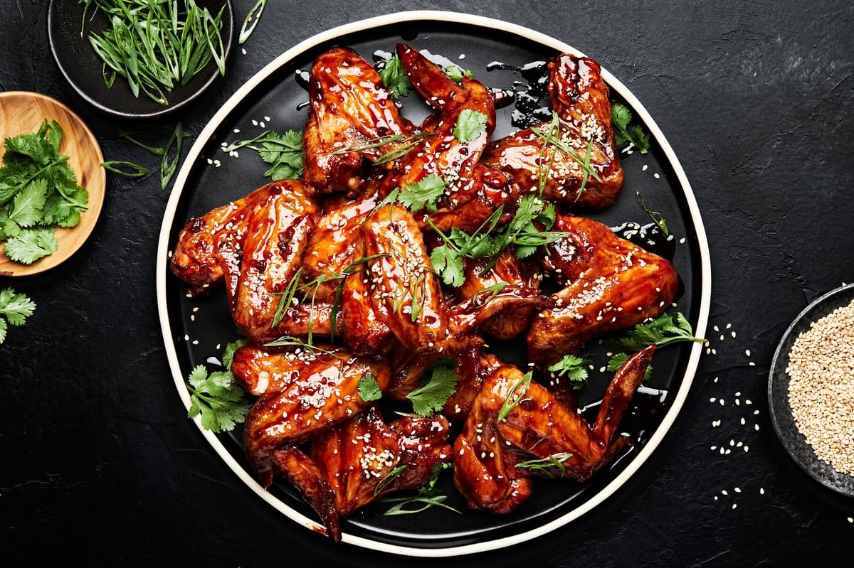 Korean Style Baked chicken wings sprinkled with cilantro, green onions and sesame seeds on a serving platter