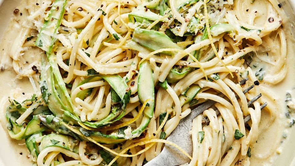Pasta al Limone with Asparagus topped with pecorino Romano, lemon zest, and pepper in a pasta bowl with a fork