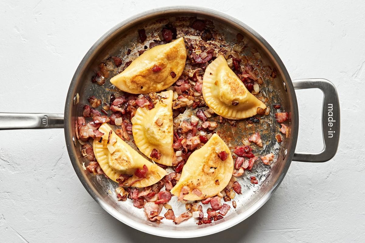boiled pierogi's being fried in a skillet with onions and bacon