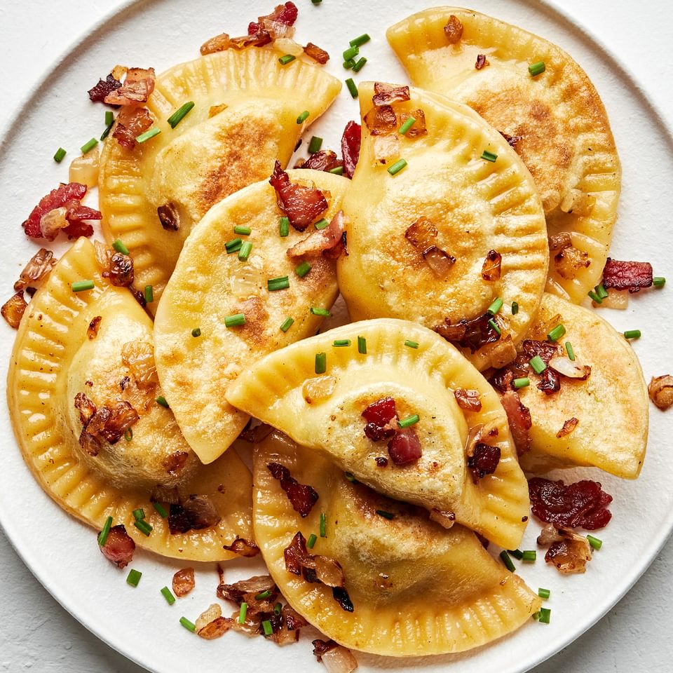 a plate of homemade pierogis: potato filled dumplings boiled then fried in a skillet with onion and bacon