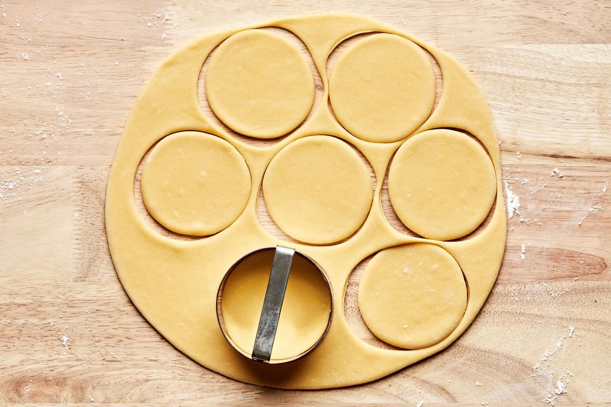 rolled pierogi dough on a wood surface being cut into 3 inch circles with a biscuit cutter