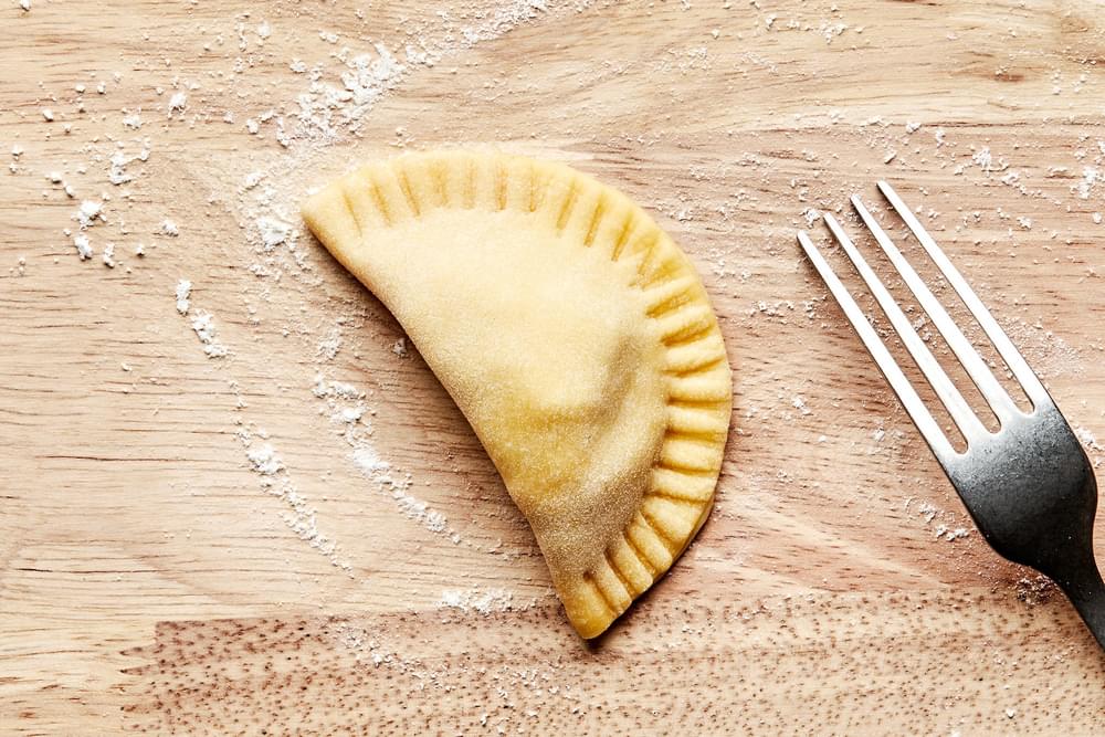 pierogi dough folded in half filled with potato filling and being crimped around the edges with a fork